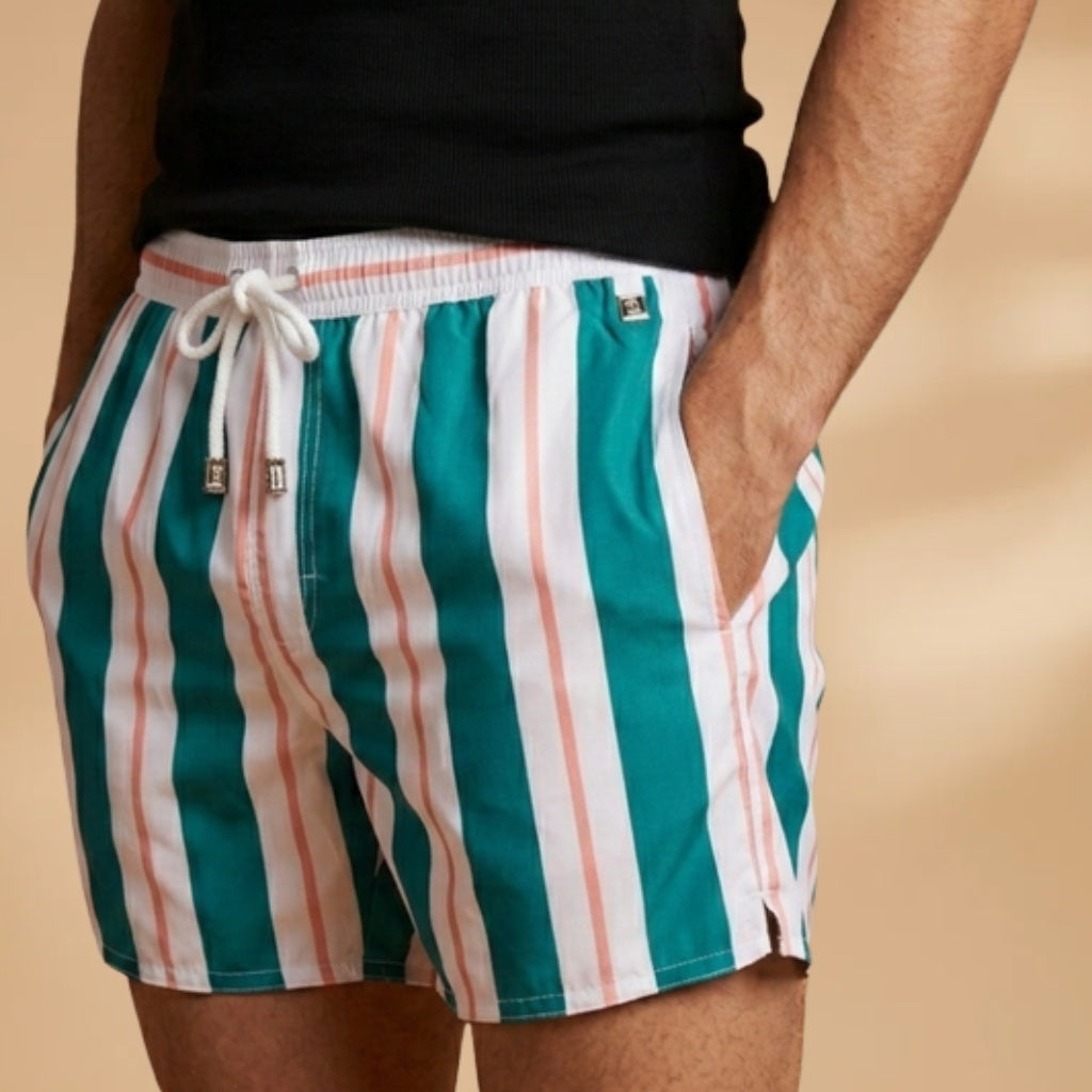 Homem a usar calções de banho listrados na praia. Roupa de banho masculina, ideal para o verão e piscina.