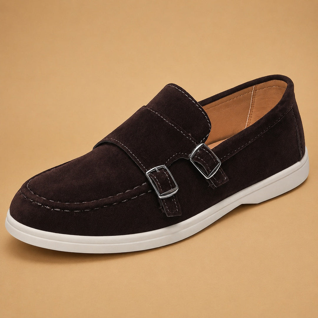 Mocassim masculino slip-on lateral, mostrando a camurça macia e fivela dupla sofisticada.